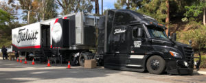 A large black semi-truck with the Titleist logo and 'Tour Truck' text displayed prominently on the side, parked in a wooded a
