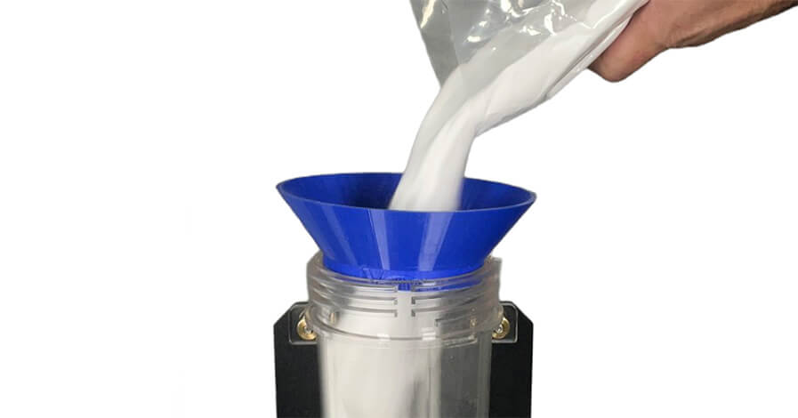 A hand pouring a white powdery substance into a blue funnel-shaped container atop a sandblaster.